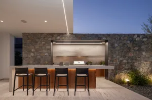Modern outdoor kitchen featuring concrete countertops and stone walls with a grill and seating area.