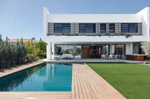 A modern residential house with a pool, wooden deck, and a green lawn.