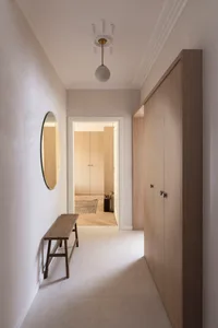 A minimalist corridor with wooden walls and floors, featuring a round mirror, a wooden bench, and a ceiling light fixture.