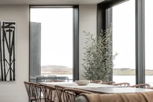 A minimalist dining room with wood furnishings and a large window with greenery outside.