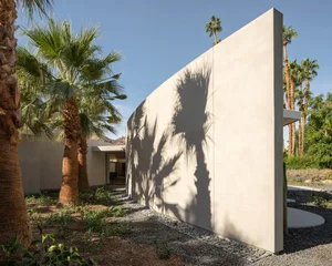 Concrete exterior walls of a minimalist residential house with palm tree shadows.