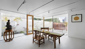 A minimalist tea room featuring a wooden table, chairs, and a view of a serene outdoor area with a white wall and wooden fenc