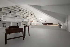 A minimalist living space with white walls, shelves, and furniture in white and dark wood.