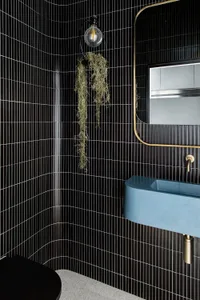 A modern bathroom with black vertical-striped tiled walls, a blue sink, and decorative hanging plants.