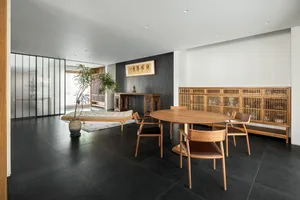 A modern living room with wooden furniture, black tiles, white walls, and a glass wall.