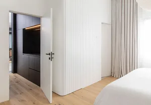 A modern minimalist bedroom featuring white accent wall and wooden flooring.