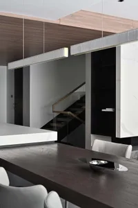 Modern minimalist dining room featuring metallic lighting above a wooden table with white chairs and a glass staircase in the