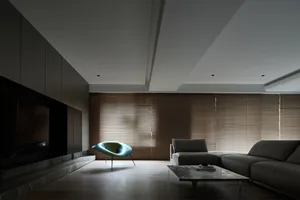 A minimalist living room with a grey sofa, coffee table, and unique armchair, featuring brown wood blinds and a dark wood flo
