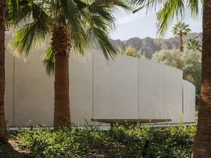 A modern residential exterior featuring a curved concrete wall and lush greenery.