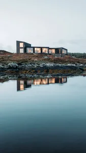 Modern waterfront home with illuminated windows reflecting in the still water at night.