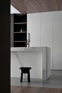Modern minimalist kitchen with white marble countertops and black stools.
