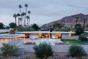 Modern residential house with concrete exterior and outdoor patio featuring a pool and lounge chairs.