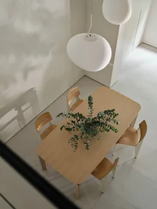 A minimalist dining room featuring a wooden table with a plant arrangement, surrounded by chairs and illuminated by hanging l