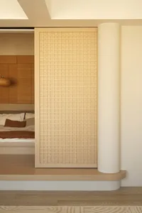 Modern minimalist interior space with a light-colored tiled wall and wooden columns.