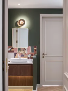 Modern bathroom featuring colorful ceramic tiles on the backsplash, illuminated by a round sconce light fixed to the wall.