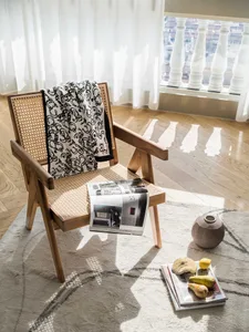 Modern living room featuring wood and cane furniture, with a blanket, a magazine, and a vase with fruits on a patterned rug.