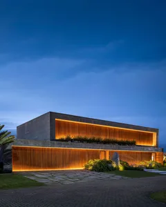A modern minimalist house with concrete facade at night, illuminated by warm indoor lighting.
