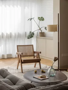 A modern minimalist living room featuring a wooden armchair, a round wooden table with fruits and a magazine, and a floor lam
