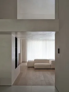 Modern minimalist residential interior with concrete walls, wood flooring, and a large window allowing natural light to enter