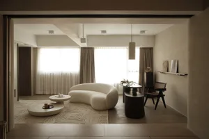 A modern living room featuring a curved white sofa, round coffee tables, and neutral-toned decor.