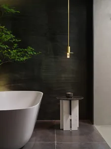 A modern minimalist bathroom featuring a freestanding white bathtub and a suspended brass pendant light hanging from a dark g