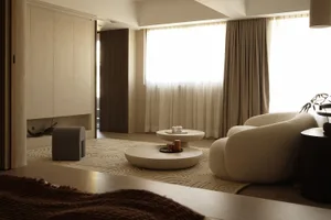 A minimalist living room featuring neutral-toned furniture and decor, with large windows and a comfortable seating area.