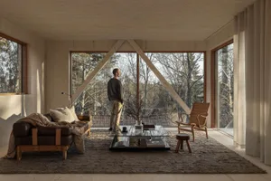 A minimalist living room with wooden beams and large windows showcasing a forest view.