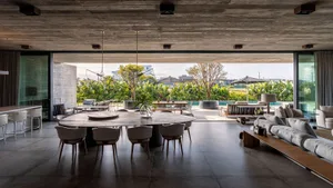 Modern, minimalist residential interior with concrete walls and floor, large windows, and outdoor patio.