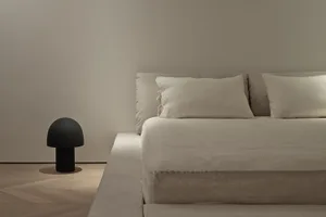 A minimalist white bedroom featuring a fabric bed with a simple, elegant headboard and side table.