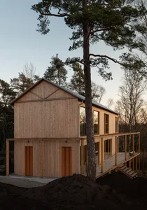 Modern house exterior with wooden siding and large windows surrounded by trees.