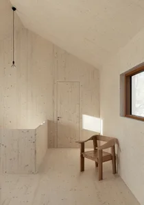 A minimalist wooden room with a chair, door, and pendant light hanging from the ceiling.