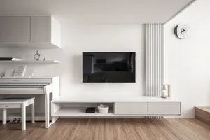 Modern living room with white walls, furniture, and floor, featuring a white piano, a TV mounted on the wall, and a white clo