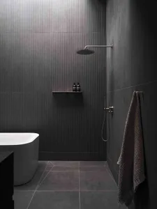 Modern minimalist bathroom with dark tiles and concrete floor, featuring a freestanding tub and walk-in shower.