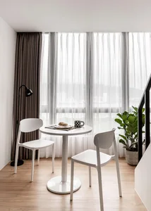 A minimalist dining area featuring a round white table with a plate, mug, and bread, surrounded by two white chairs, under a 