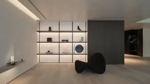A minimalist living room featuring modern metal shelving with a single black sculptural chair, illuminated by hidden lighting