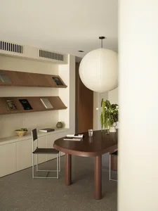 A minimalist living room with wooden furniture, a round pendant light, and a bookshelf.