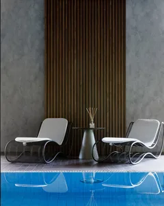 A minimalist poolside seating area featuring modern metal chairs and a table with a vase of reeds, placed adjacent to a swimm