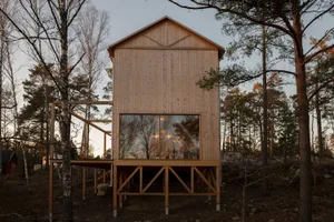 Modern minimalist wooden house surrounded by trees with a large window.