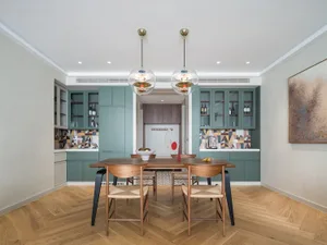 A modern kitchen dining room with wooden floors, green cabinetry, and glass pendant lights.