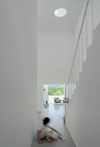 Minimalist white interior design featuring a hallway with stairs and floor-to-ceiling windows.