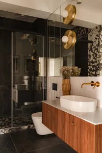Modern bathroom featuring a white oval sink, wooden vanity, and black composite tiles on the floor and walls.