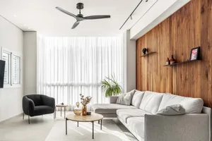 A modern living room featuring wood-paneled walls, a concrete floor, and a comfortable grey sofa with white cushions, illumin