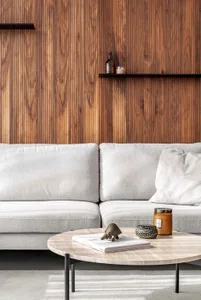 A modern living room with a white couch, wooden paneling, and a coffee table with decorative items.