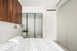 A minimalist bedroom featuring glass walls and a white bed with wooden accents.