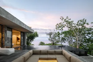 A modern residential exterior featuring a concrete house with large windows and an infinity pool overlooking the ocean.