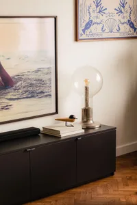 A stylish mid-century modern sideboard with a glass lamp and books on top, framed pictures on the wall, and a wooden floor.