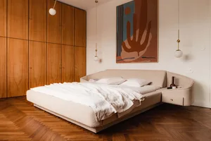 A modern bedroom with a white fabric bed, wooden wardrobe, and hanging lights.