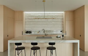 A modern kitchen with a marble countertop, wooden cabinets, and black stools.