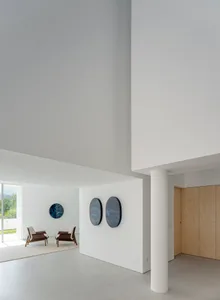 A modern living room with minimalist design features, including white walls, concrete flooring, and circular artworks on the 