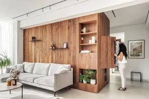 A modern living room featuring a grey sofa, wooden cabinets, and a large window with white curtains.
